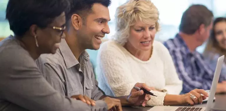 Group of people at a table discussing something on a laptop